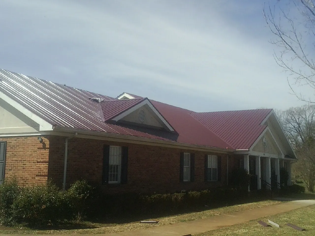 Red metal roof with gabled entries on a long brick building, from a Hail Damage Roof Repair job in Maryville