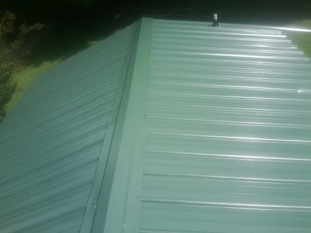 New green metal panels meeting at the ridge of a roof — Flat Roof Repair work by our crew in Maryville
